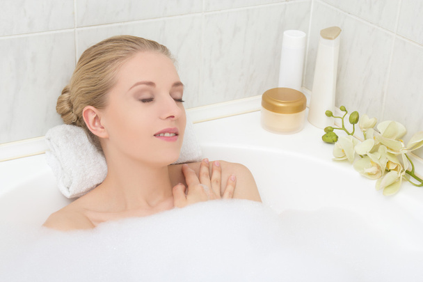 young woman lying in bath with foam and orchid flower - Photo, Image