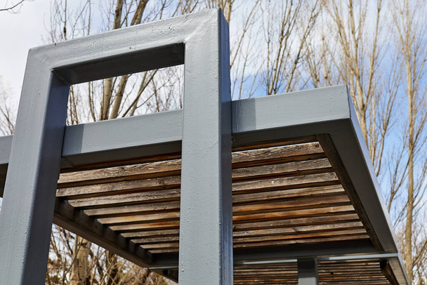 Parktaki banklar için metal ve tahtalardan yapılmış dekoratif gölgeleme yapısının bir parçası - Fotoğraf, Görsel