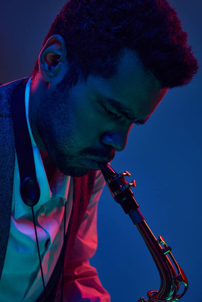 Jazz v moderní hudbě. Zblízka fotografie mladého pohledného muže hrajícího na saxofon v neonovém světle. Gelové portréty. Koncept blues, klasická instrumentální hudba, festivaly a koncerty. Reklama - Fotografie, Obrázek