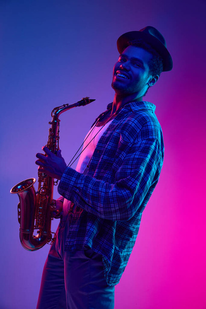 Retrato de meio-comprimento do homem afro-americano, saxofonista tocando jazz contra gradiente de fundo roxo-rosa gradiente. Conceito de jazz, blues, música instrumental de classe. Anúncio - Foto, Imagem