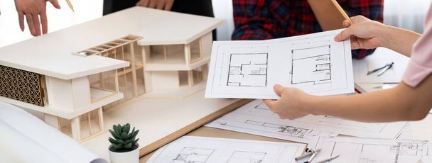 Architect team analysis and brainstorming about house construction at meeting table with house model, blueprint and architectural equipment scatter around. Creative design and teamwork. Burgeoning. - Photo, Image