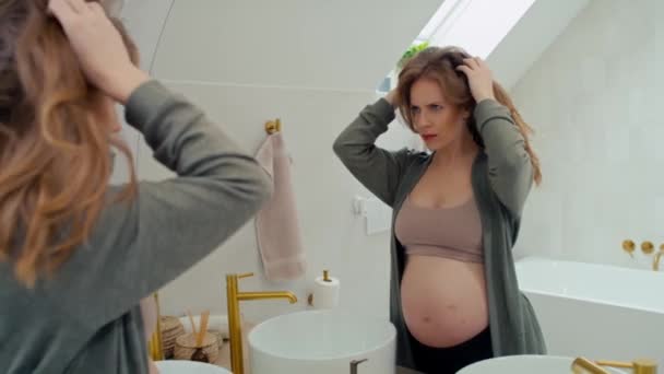 Biała kobieta w ciąży sprawdza stan włosów w lustrze - Materiał filmowy, wideo