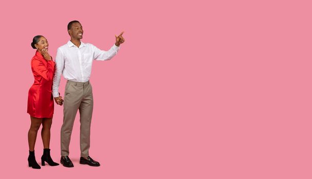 Homem preto em camisa branca apontando para o espaço livre com mulher em vestido vermelho sorrindo e olhando intrigado, lugar para propaganda, oferta ou promo, fundo rosa - Foto, Imagem