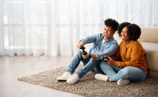 Wesoła młoda afrykańska kobieta i mężczyzna gracze grają w gry komputerowe z joystickiem, bawić się, cieszyć się wolnym czasem, w salonie wnętrza. Związek, rozrywka w domu - Zdjęcie, obraz