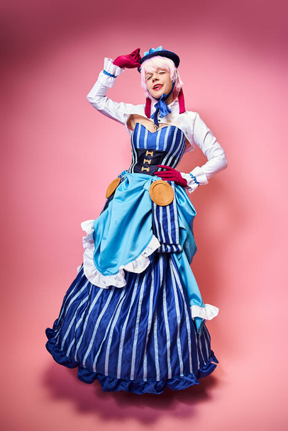 charming sexy female cosplayer in blue hat and vibrant attire looking at camera on pink backdrop - Photo, Image