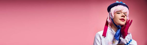 seductora cosplayer femenina en sombrero azul y ropa vívida mirando a la cámara en el fondo rosa, pancarta - Foto, Imagen