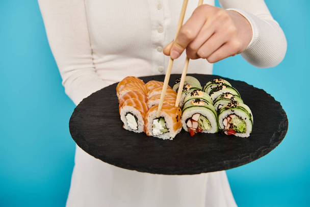 Ausgeschnittene Ansicht der schönen Frau mit einem schwarzen Teller gefüllt mit köstlichen Sushi-Rollen. - Foto, Bild