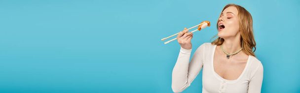 Žena s blond vlasy drží hůlky s lahodným sushi. - Fotografie, Obrázek