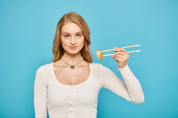 A blonde woman elegantly holds chopsticks and a delectable piece of Asian cuisine. - Foto, imagen