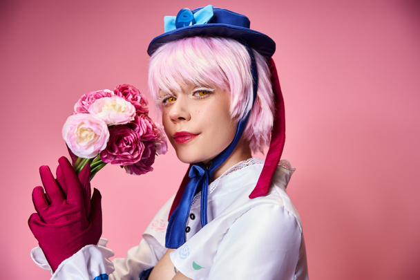 alluring cute female cosplayer in vibrant costume holding pink flowers and looking at camera - Zdjęcie, obraz