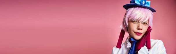 привлекательный шикарный косплеер в синей шляпе и ярком платье глядя на камеру на розовом фоне, баннер - Фото, изображение