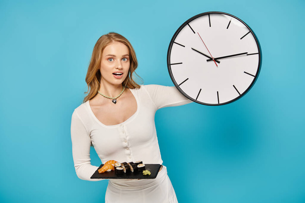 Una donna con i capelli biondi tiene un orologio in una mano e un piatto di cibo asiatico nell'altra, mostrando un equilibrio tra tempo e indulgenza.. - Foto, immagini