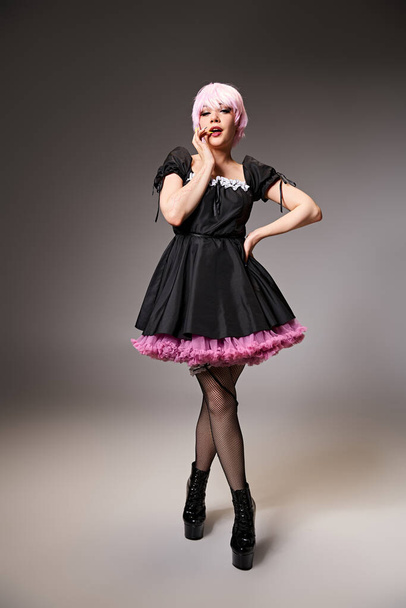 seductora mujer elegante en vestido negro con el pelo rosa personaje de anime cosplaying y mirando a la cámara - Foto, Imagen