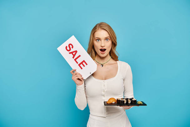 A beautiful woman with blonde hair holding a sign that says sale while posing with delicious Asian food. - Foto, Bild