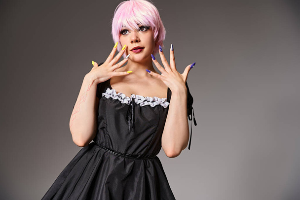 sexy female cosplayer in black dress with pink hair posing on gray backdrop and looking away - Zdjęcie, obraz