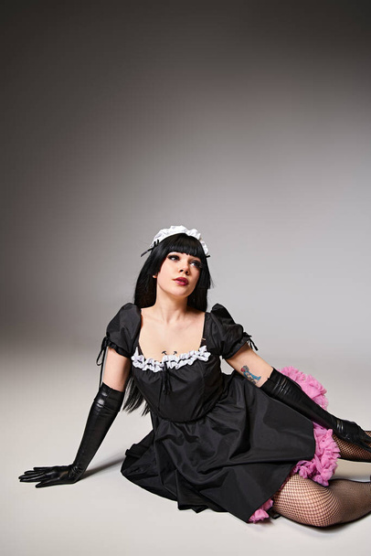 appealing sexy cosplayer in black maid costume posing actively and looking away on gray backdrop - Foto, imagen