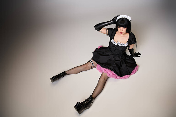 glamorous sexy female cosplayer in tempting maid costume looking at camera on gray background - Photo, Image