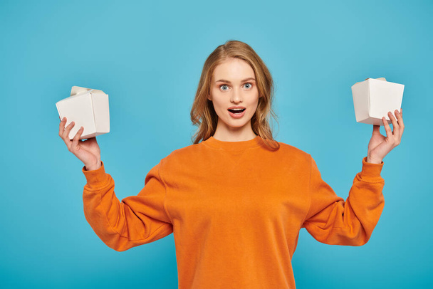 A beautiful blonde woman gracefully holds two white boxes, showcasing gourmet Asian cuisine. - Photo, Image
