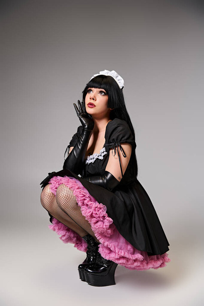 attractive young cosplayer in maid costume posing alluringly and looking away on gray backdrop - Foto, immagini