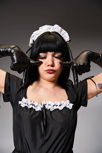 ansprechende sexy Frau in verführerischem Dienstmädchenkostüm posiert mit geschlossenen Augen und zeigt weinende Geste - Foto, Bild