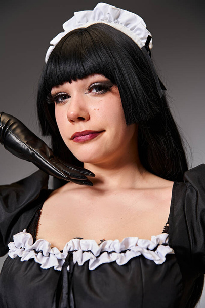 attraktive sexy Cosplayerin im verführerischen Dienstmädchenkostüm mit Blick auf die Kamera auf grauem Hintergrund - Foto, Bild