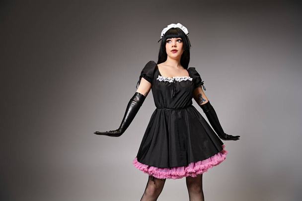 beautiful young cosplayer in maid costume posing alluringly and looking away on gray backdrop - Foto, imagen
