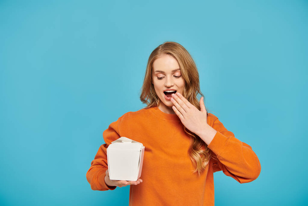 Žena s blond vlasy drží krabici asijského jídla před obličejem. - Fotografie, Obrázek
