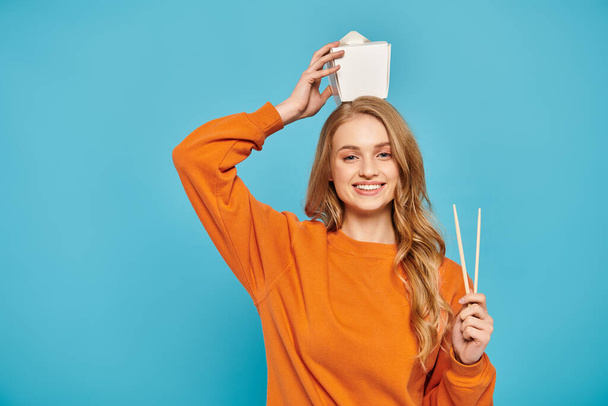 A blonde woman in an orange sweater posing serenely with Asian food. - Φωτογραφία, εικόνα