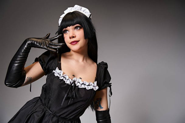 appealing young cosplayer in maid costume posing alluringly and looking away on gray backdrop - Photo, Image