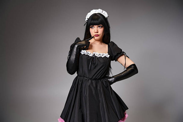 atractivo cosplayer joven en traje de criada posando seductor y mirando hacia otro lado en el fondo gris - Foto, imagen