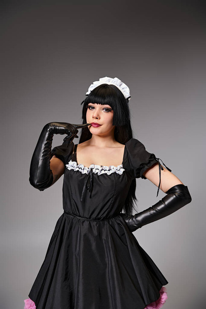 atractivo sexy cosplayer femenino en tentador traje de criada mirando a la cámara sobre fondo gris - Foto, imagen
