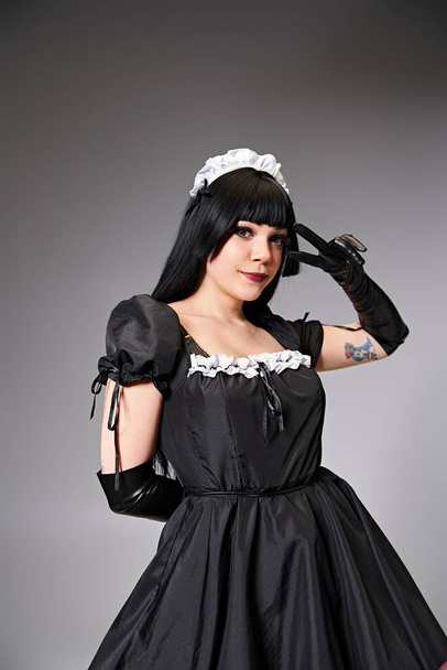 attraktive Frau cosplaying sexy Dienstmädchen mit schwarzen Handschuhen zeigt Friedensgeste und Blick in die Kamera - Foto, Bild