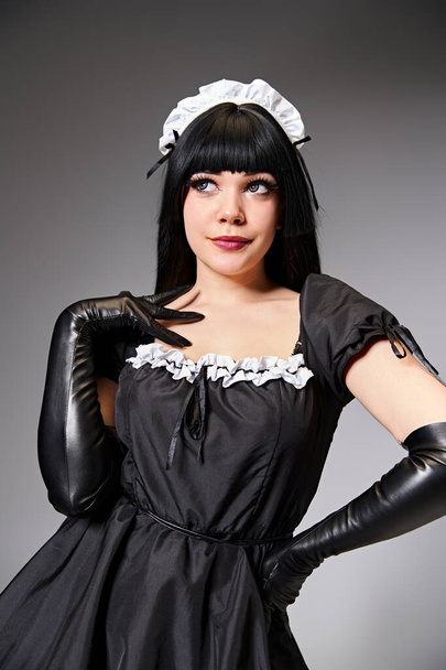 sexy cosplayer atractivo en traje de criada posando seductor y mirando hacia otro lado en el fondo gris - Foto, imagen