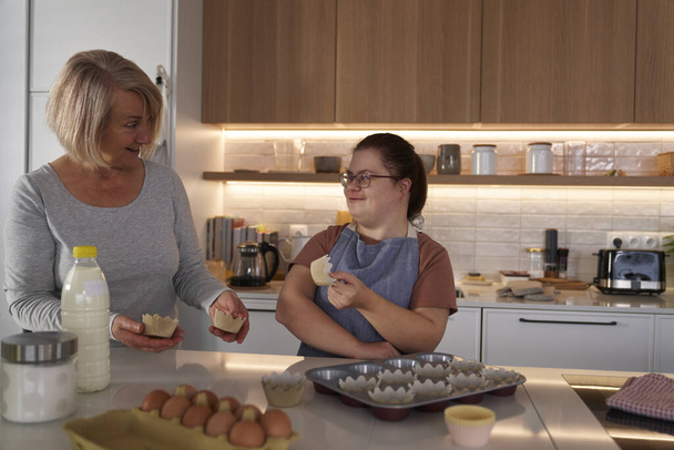 Síndrome de Down mujer y madre preparando cupcakes caseros - Foto, imagen