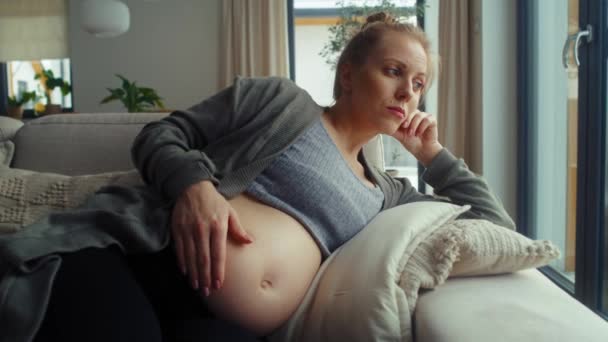 Αγχωμένη έγκυος γυναίκα ξαπλωμένη στον καναπέ και αγγίζοντας την κοιλιά της - Πλάνα, βίντεο