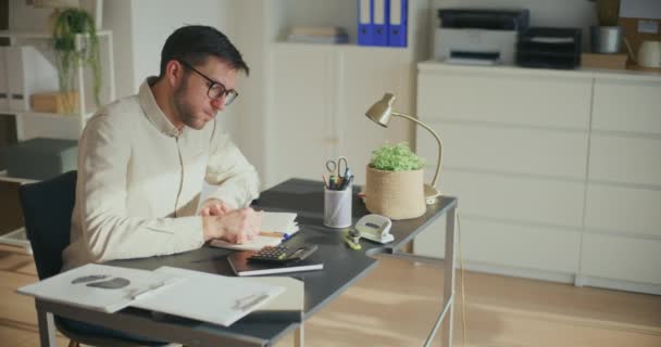 Uitgeputte jonge mannelijke ondernemer die pauze neemt terwijl hij aan zijn bureau zit - Video