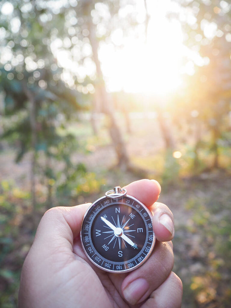 Lähikuva kompassin naisen kädessä metsän auringonlaskun aikaan taustana. Käsite maailman matkailupäivä, etsivät oikeita suuntia ja Travel - Valokuva, kuva