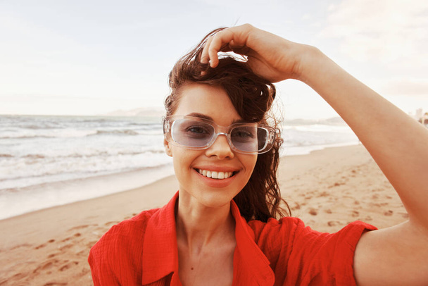 Mulher sorridente abraçando a liberdade, desfrutando do pôr do sol colorido na praia - Foto, Imagem