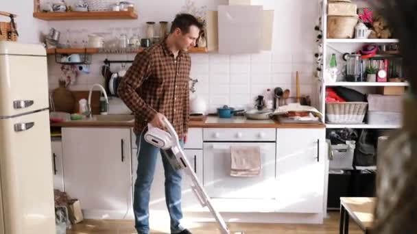 Un uomo caucasico di mezza età aspira un appartamento con un aspirapolvere portatile in cucina. - Filmati, video