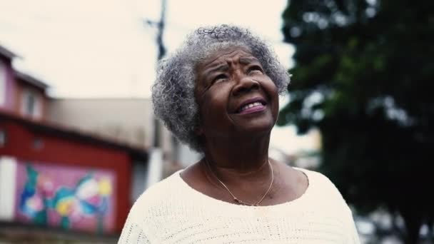 Spiritual African American lady standing in city street gazing upwards at sky with HOPE and FAITH. One Grateful black lady with gray hair in 80s looking skywards - Footage, Video