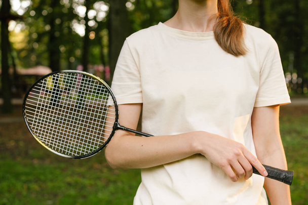 Großaufnahme einer jungen Frau im T-Shirt, die einen Badmintonschläger in der Hand hält. Konzept von Outdoor-Sportspielen, Wettbewerb und Zeitvertreib - Foto, Bild
