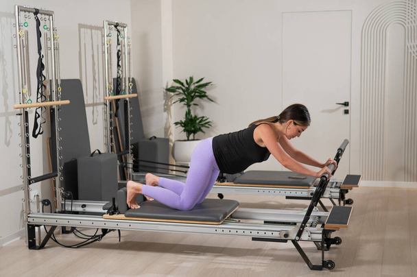 A pregnant woman does a plank on a reformer machine. Perinatal yoga - Photo, image