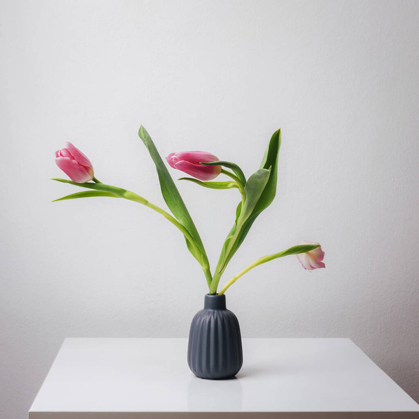 Vase mit Tulpen auf weißem Tisch vorhanden. Frühlingsfestlicher Hintergrund. - Foto, Bild