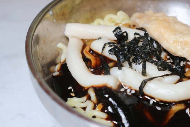 Крупним планом корейська їжа Rabboki (Смажений рисовий пиріг та Ramen Noodle) увінчана норі (водорості) на металевій мисці - Фото, зображення
