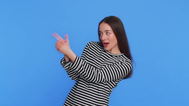 Καυκάσια γυναίκα που δείχνει τριγύρω με μια χειρονομία πιστολιού που δείχνει σίγουρη να κάνει επιλογή πυροβολώντας με το πιστόλι χειρός ακριβώς πάνω στο στόχο. Νεαρή κοπέλα απομονωμένη σε μπλε φόντο σε εσωτερικούς χώρους. Διαφήμιση - Πλάνα, βίντεο