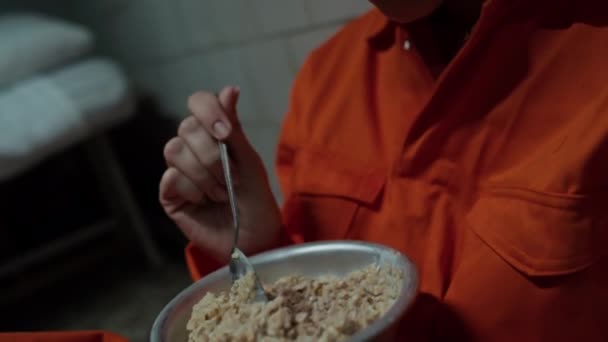 Vista de cerca de una reclusa asquerosa comiendo avena de un tazón de acero mientras está sentada en la celda de la prisión - Metraje, vídeo
