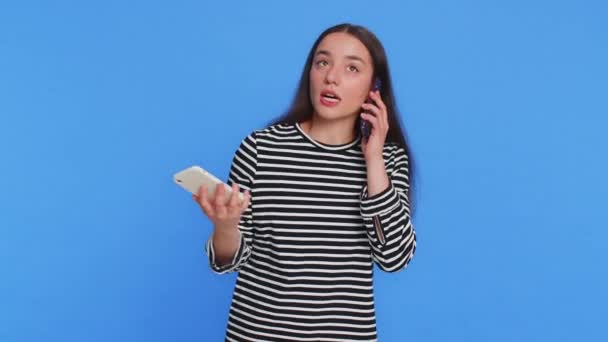 Podrážděný nervózní vystresovaný běloška mluví křičí do dvou mobilních telefonů s konverzace konflikt spor stížnost spor diskutovat o vyřešení problému. Mladá dívka izolované na modrém pozadí - Záběry, video