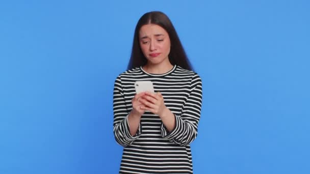 Rozrušený smutný běloška použít smartphone psaní prohlížení, hrát hru, prohrává, překvapen náhlými výsledky loterie smůlu ztráta štěstí neštěstí zprávy. Pěkná krásná dívka izolované na modrém pozadí - Záběry, video