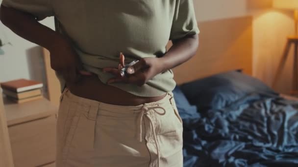 Orta ölçekli, genç Afrikalı Amerikalı bir kadın yatak odasında duruyor, cilt kıvrımlarını çimdikliyor ve karın bölgesine insülin enjekte ediyor. - Video, Çekim