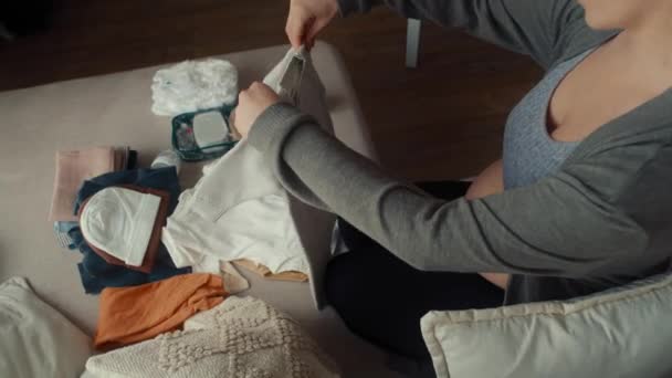 Visão de alto ângulo da mulher grávida dobrando roupas de bebê - Filmagem, Vídeo